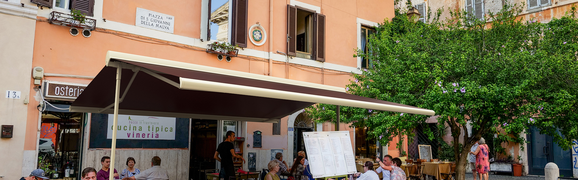 Rome, Italy, Jun 12 - A typical small restaurant with characteristic outdoor tables in Piazza San Giovanni della Malva, in the ancient Trastevere district, the most loved and visited roman district by the tourists of the ethereal city, with the facades of the buildings in warm pastel tones and large pedestrian areas.