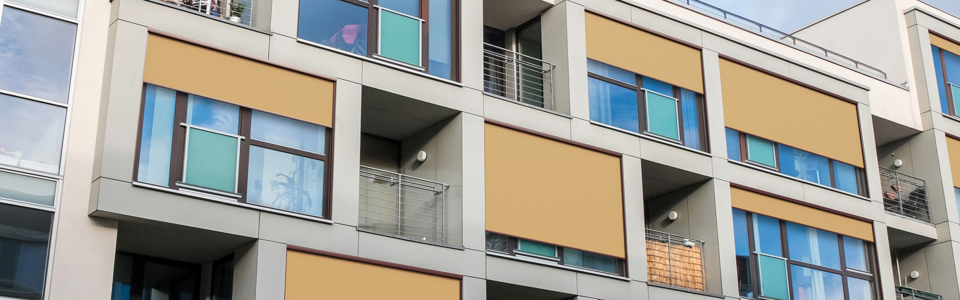 Low Angle Exterior View of Contemporary Low Rise Apartment Building with Small Balconies and Large Windows with Cloudy Blue Sky in Background