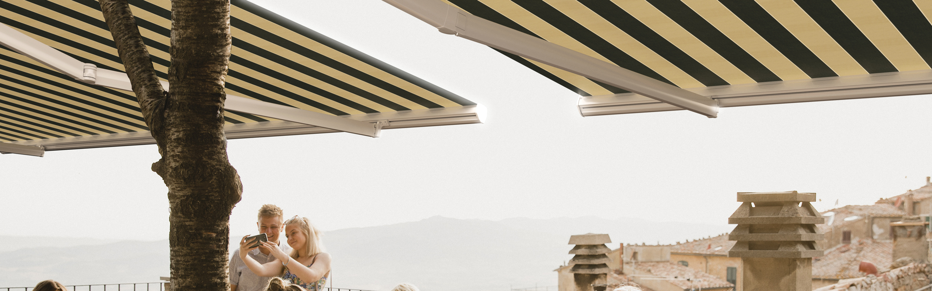 Large group of people sitting and standing on a rooftop terrace of a restaurant in Volterra. Three female friends are making a celebratory toast with their glasses of wine.